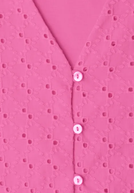 Close-up van een roze top met ajourborduurwerk en kleine knoopjes langs de V-hals.
