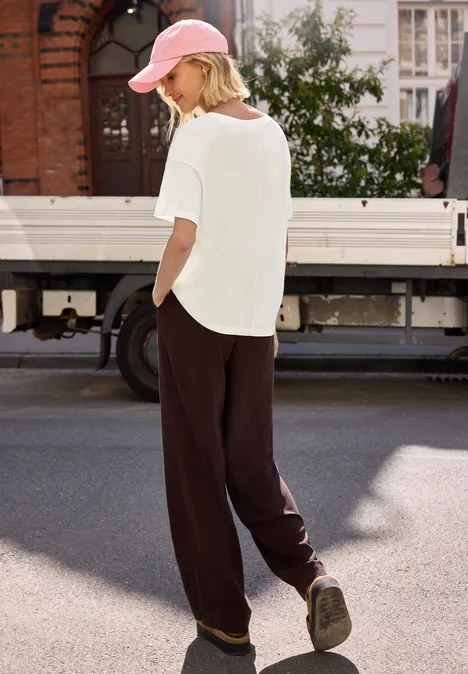 Frau in weißem T-Shirt, Baseballcap und weiten dunklen Hosen spaziert an einem LKW vorbei.