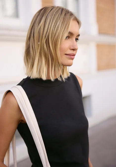 Basic Top mit Turtle Neck in Unifarbe Black Blonde Frau mit schulterlangem Haar trägt schwarzes Top und weiße Tasche, läuft in der Stadt