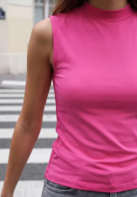 Basic Top mit Turtle Neck in Unifarbe ruby raspberry Frau in rosa ärmellosem Top und Jeans steht auf einem Zebrastreifen.