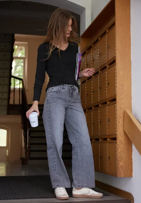 Frau in schwarzem Oberteil und grauen Jeans holt Post aus dem Briefkasten.