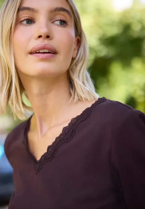 Blondine in donkerpaarse V-hals met kant kijkt buiten omhoog.