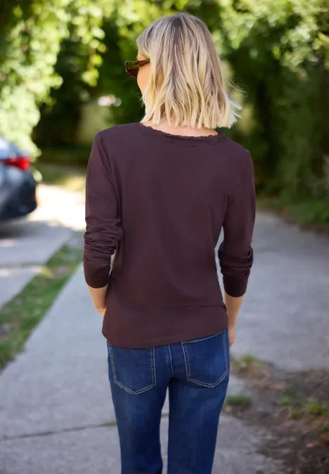 Achteraanzicht van een blonde vrouw met zonnebril, bruin shirt en jeans op een voetpad.