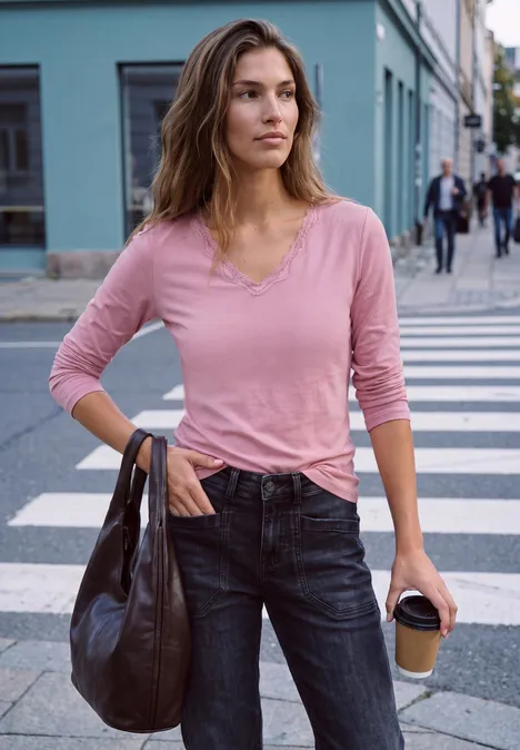 Eine Frau in pinkem Shirt und Jeans überquert mit Kaffeebecher in der Hand eine Straße.
