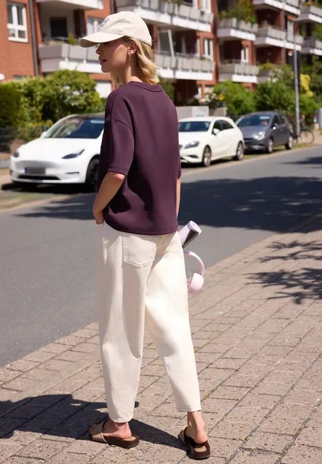 Person in lila Shirt und weißer Hose mit Cap läuft auf dem Bürgersteig vor geparkten Autos und Wohnhäusern