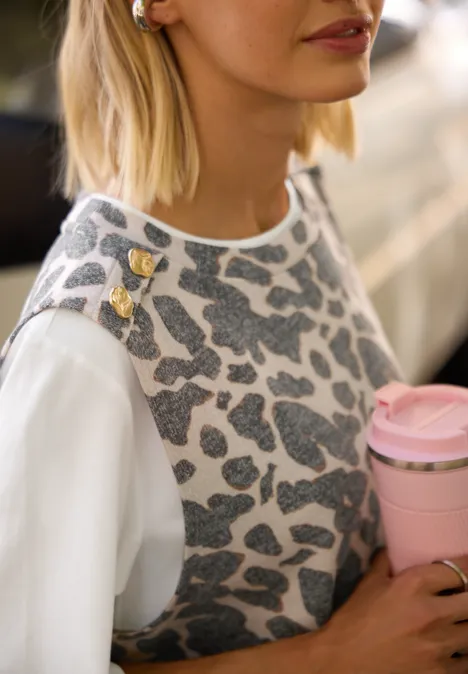 2-in-1 Shirt mit Knöpfen und Leo-Muster Black Frau trägt graues Leo-Stricktop über weißem Shirt, mit goldenen Schulter-Pins und hält rosa Kaffeebecher.