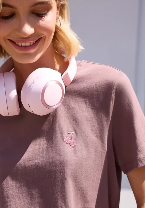 Person mit rosa Kopfhörern und T-Shirt mit kleinem Kirschlogo