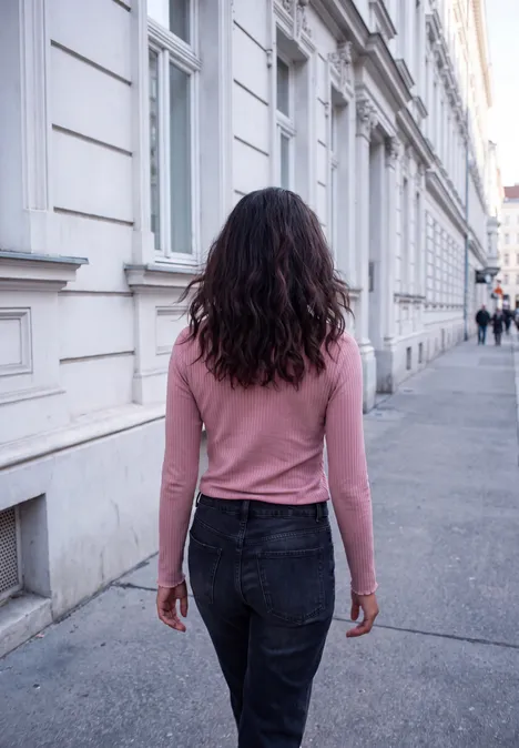 Langarm Shirt mit Turtle Neck pearly rose Eine Frau mit rosa Oberteil und Jeans geht an weißen Fassaden entlang, von hinten gesehen.