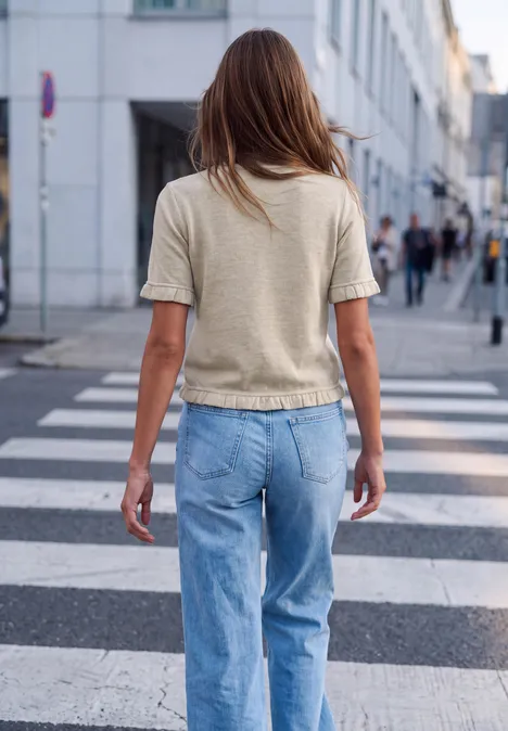 Kurzarm Shirt mit Rundhals und Rüschen creamed sand mel. Eine Frau in Jeans und T-Shirt geht über einen Zebrastreifen in der Stadt, seitliche Ansicht von hinten.