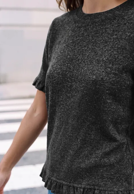 Kurzarm Shirt mit Rundhals und Rüschen inked grey mel. Frau trägt dunkelgraues, leicht glitzerndes T-Shirt mit kurzen Rüschenärmeln und Rüschenbund.