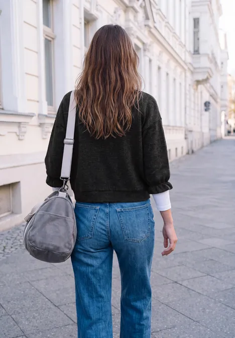 Eine Frau in blauer Jeans und schwarzem Pullover geht mit grauer Tasche eine Straße entlang.