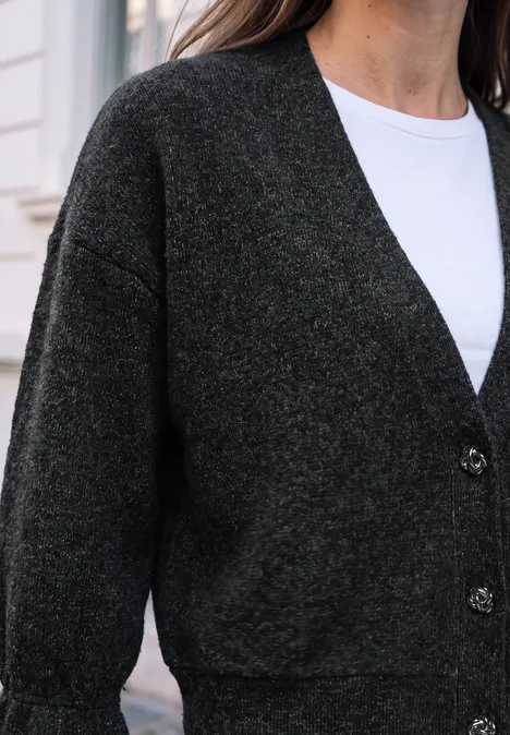 Eine Frau trägt einen dunkelgrauen Cardigan über weißem Shirt.