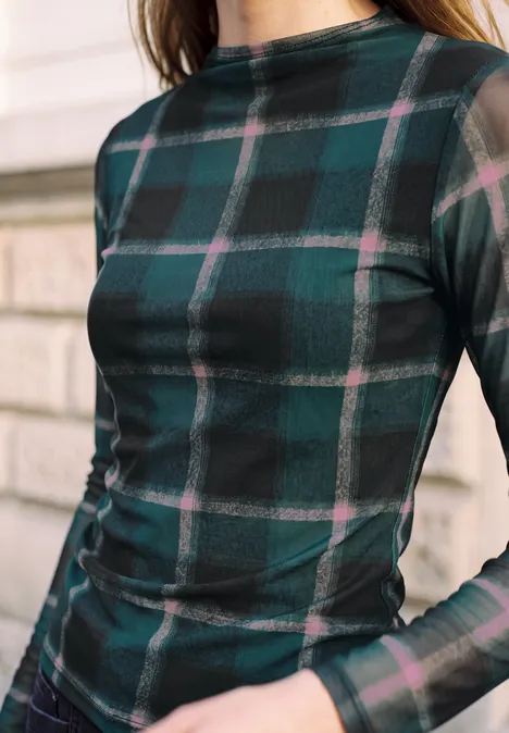 Nahaufnahme des Oberkörpers einer Person in einem transparenten grün-karierten Langarmshirt.