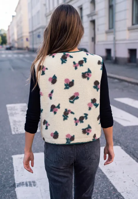 Femme de dos traversant un passage piéton, vêtue d'une veste crème à motifs fraises en milieu urbain.