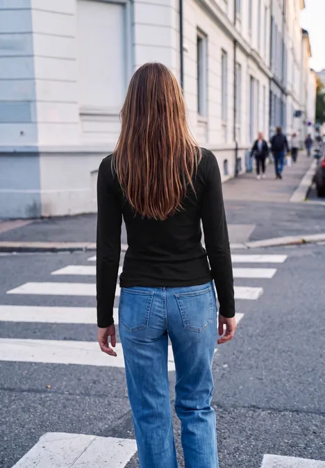Eine Frau in Jeans und schwarzem Oberteil geht über einen Zebrastreifen in einer städtischen Straße.