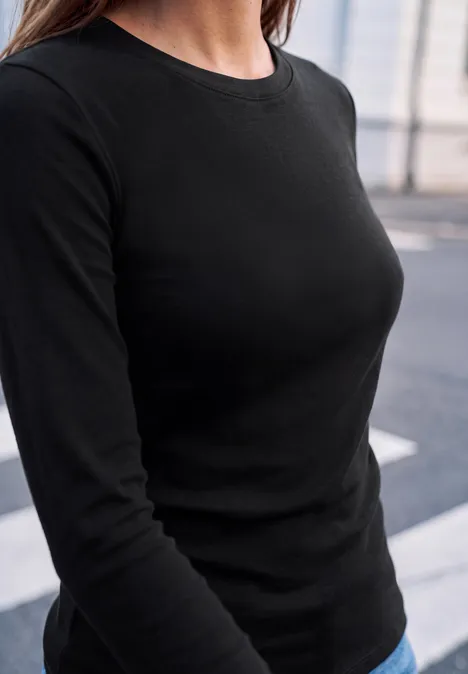 Eine Person trägt ein schwarzes, eng anliegendes Langarmshirt vor unscharfem Stadt-Hintergrund.
