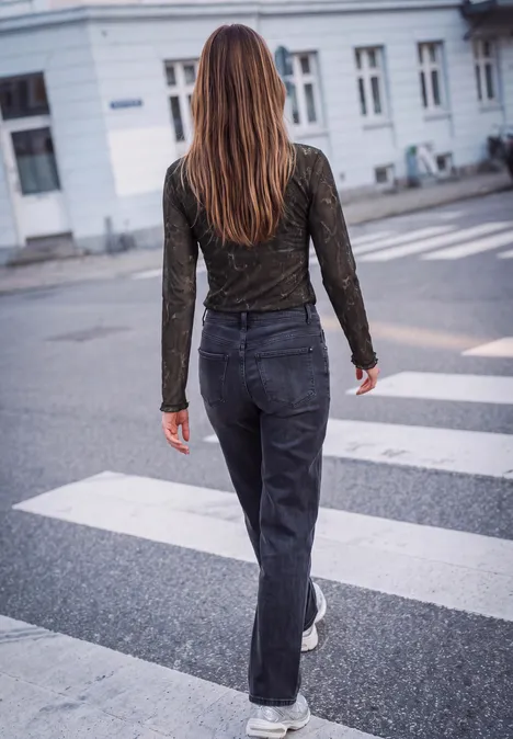 Een vrouw met lang haar loopt van achteren over een zebrapad in een donkere jeans en top in de stad.