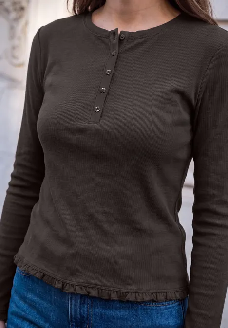 Eine Person trägt ein langärmeliges, braunes Shirt mit Knopfleiste am Ausschnitt und Jeans.