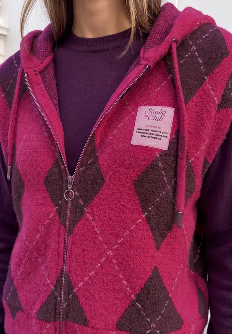 Person in rosafarbenem Rauten-Kapuzenpullover mit Reißverschluss über dunklem Oberteil.