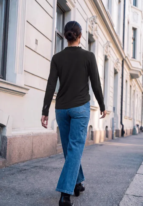 Eine Frau geht von hinten auf einem Gehweg entlang, flankiert von klassischen Gebäuden.