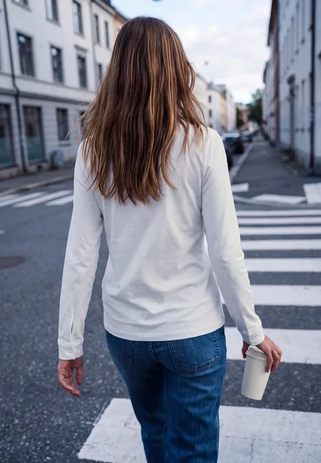 Langarm Shirt mit Rundhals und Rüschen off white Frau in weißem Shirt und Jeans überquert mit Kaffeepappbecher einen Zebrastreifen.