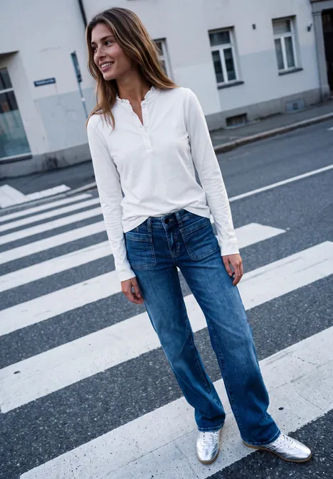 Langarm Shirt mit Rundhals und Rüschen off white Frau mit weißer Bluse und Jeans steht lächelnd auf einem Zebrastreifen in der Stadt.