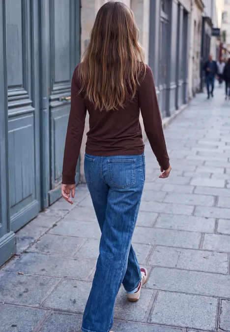 Langarm Shirt mit Rundhals und Rüschen russet red Eine Frau in Jeans und braunem Oberteil geht eine gepflasterte Straße entlang, aufgenommen von hinten.