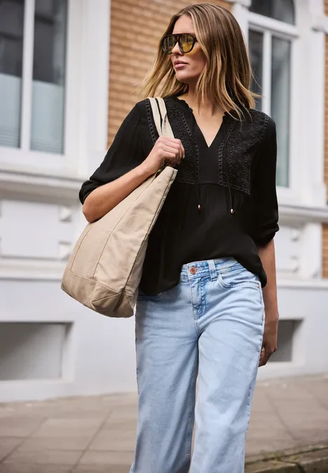 Een vrouw in een zwart shirt en jeans met tas loopt over straat.