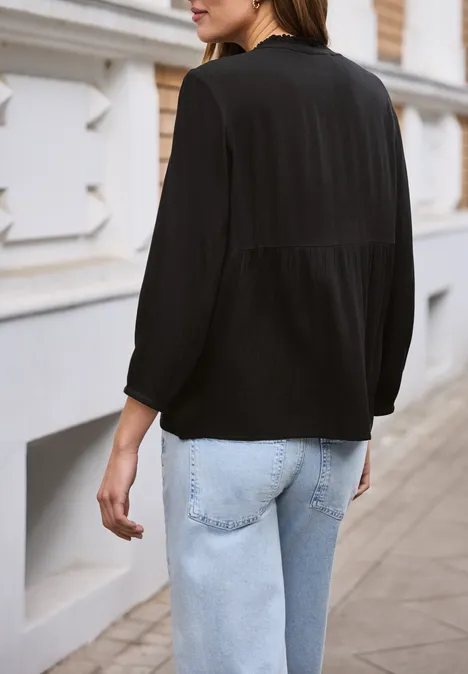 Vrouw van achteren in zwarte blouse en lichtblauwe spijkerbroek, lopend langs een gevel.