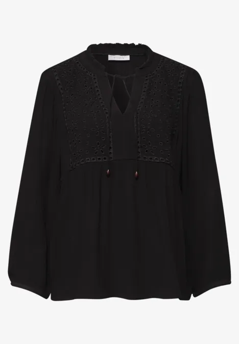 Zwarte blouse met lange mouwen, kanten details en een striksluiting bij de hals.