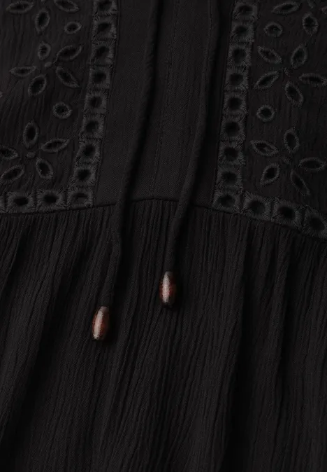 Zwarte jurk of top met ajourborduursel, gerimpelde stof en koordjes met bruine houten kralen.