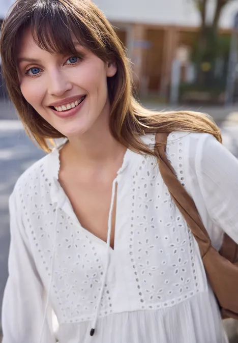 Vrouw in witte zomerse blouse met tas over de schouder, lopend buiten.