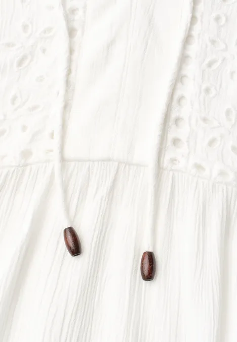 Witte katoenen stof met opengewerkt borduurwerk en koord met twee houten kralen.
