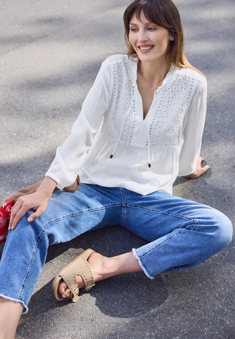 Vrouw zit op asfalt in een witte blouse en blauwe jeans, met sandalen.