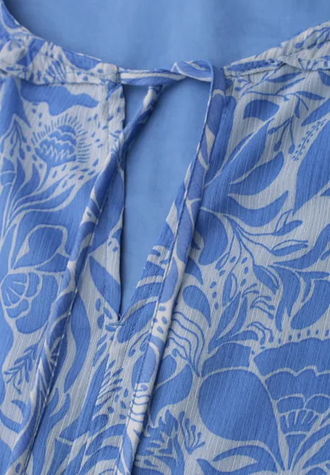 Blauwe top met wit bloemenpatroon en V-hals, afgewerkt met een strikkoord.