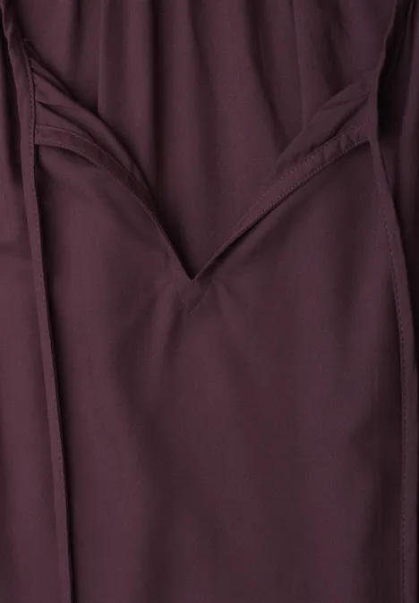 Close-up einer dunkelroten Hose mit sichtbarer Tasche und Nahtdetail.