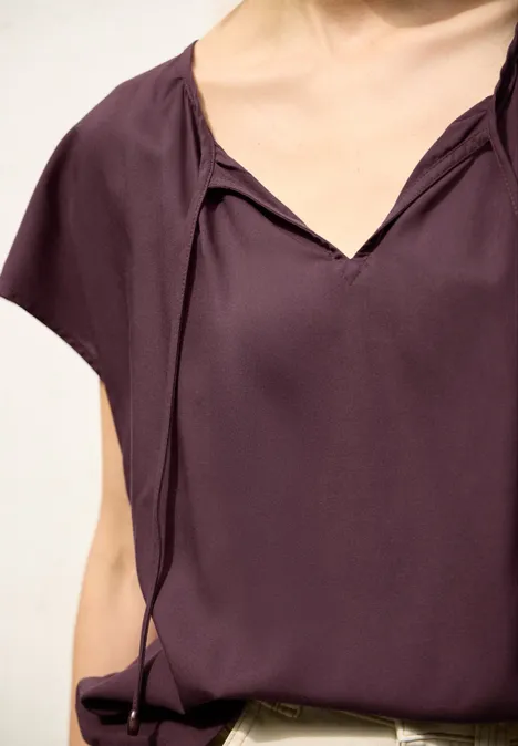 Lila Kurzarm-Bluse mit V-Ausschnitt und dekorativen Schlaufenbändern.