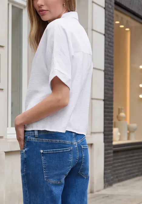 Frau mit weißem Hemd und blauen Jeans von der Seite auf der Straße.