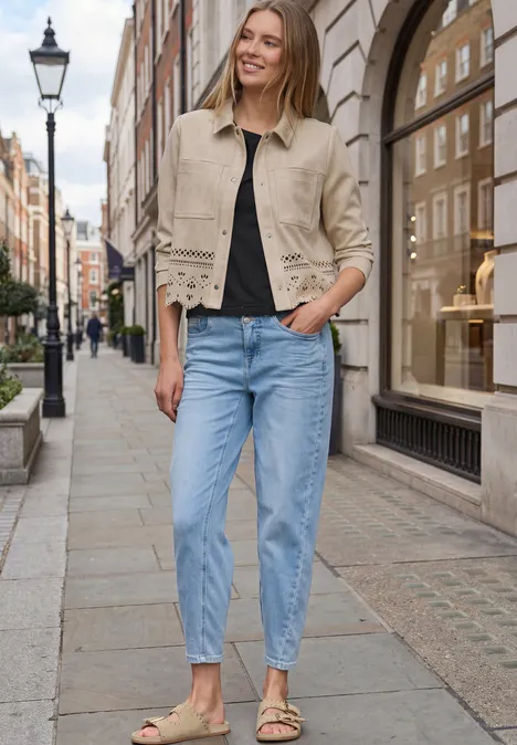 Frau in beiger Jacke und blauen Jeans geht lässig eine gepflasterte Einkaufsstraße entlang.
