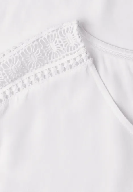 Haut blanc orné d'une fine dentelle à l'épaule.