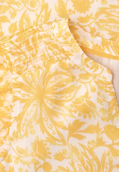 Nahaufnahme eines gelben Kleidungsstücks mit weiß-gelbem, floralem Muster und Tasche.