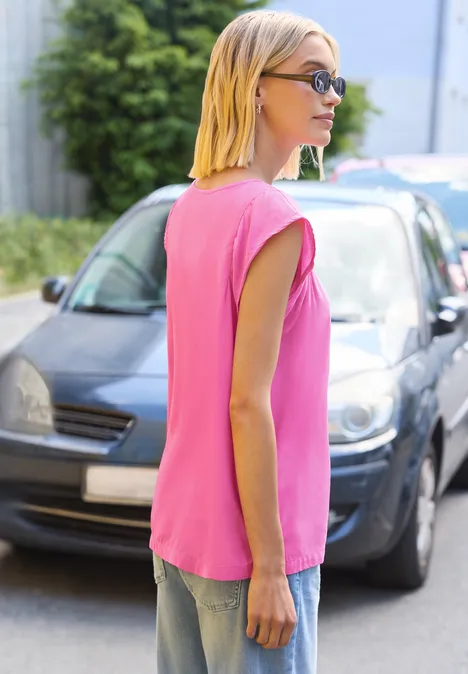 Une femme en haut rose sans manches est vue de profil près d'une voiture garée sur le trottoir.