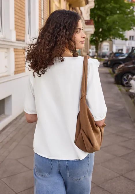 Kurzarm Bluse mit Volant-Details White Eine Frau mit lockigem Haar, weißer Bluse und brauner Tasche geht eine Straße entlang.