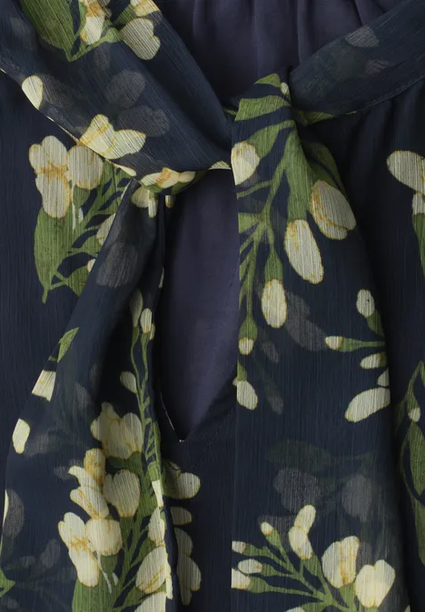 Dunkelblauer Stoff mit gelbweißen Blumen und grünen Blättern, Detail eines Oberteils mit Schlitz und Knoten.