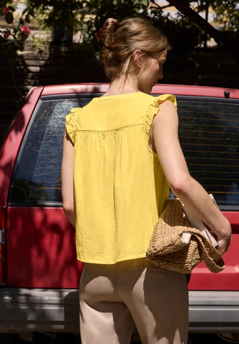 Blusenshirt mit Split Neck und Tape-Details snap yellow Eine Frau mit gelbem Top und Strohhandtasche steht vor einem roten Auto.