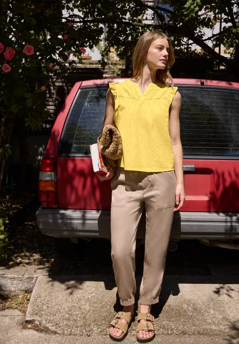 Blusenshirt mit Split Neck und Tape-Details snap yellow Eine Frau in gelbem Top und hellen Hosen steht vor einem roten Auto und hält eine Handtasche.