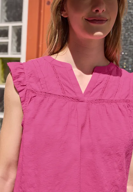 Blusenshirt mit Split Neck und Tape-Details simply pink Frau im pinken ärmellosen Oberteil mit Rüschen und V-Ausschnitt im Freien vor einem Gebäude.