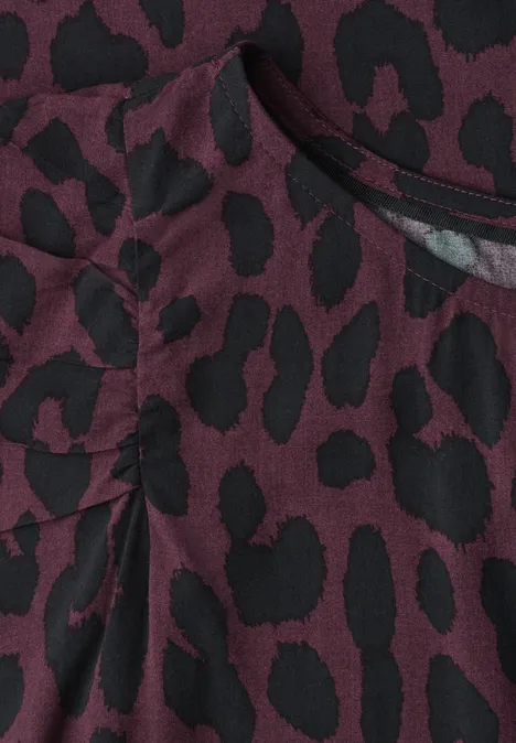 Nahaufnahme eines weinroten Stoffs mit schwarzem Leopardenmuster und Falten-/Taschendetail