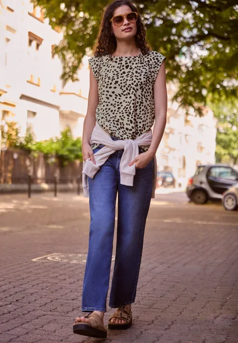 Blouse met afhangende schouders en luipaardprint Black Vrouw in modieus luipaardshirt en jeans staat ontspannen op een zonnige straat.