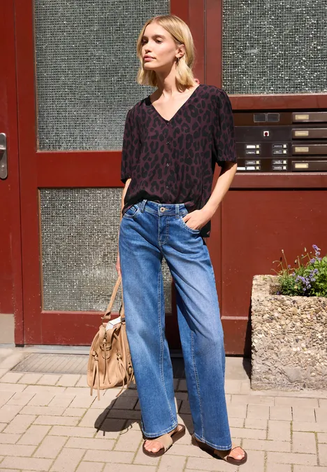 Frau steht vor Haustür, trägt Leo-Print-Shirt, weite Jeans und Handtasche.